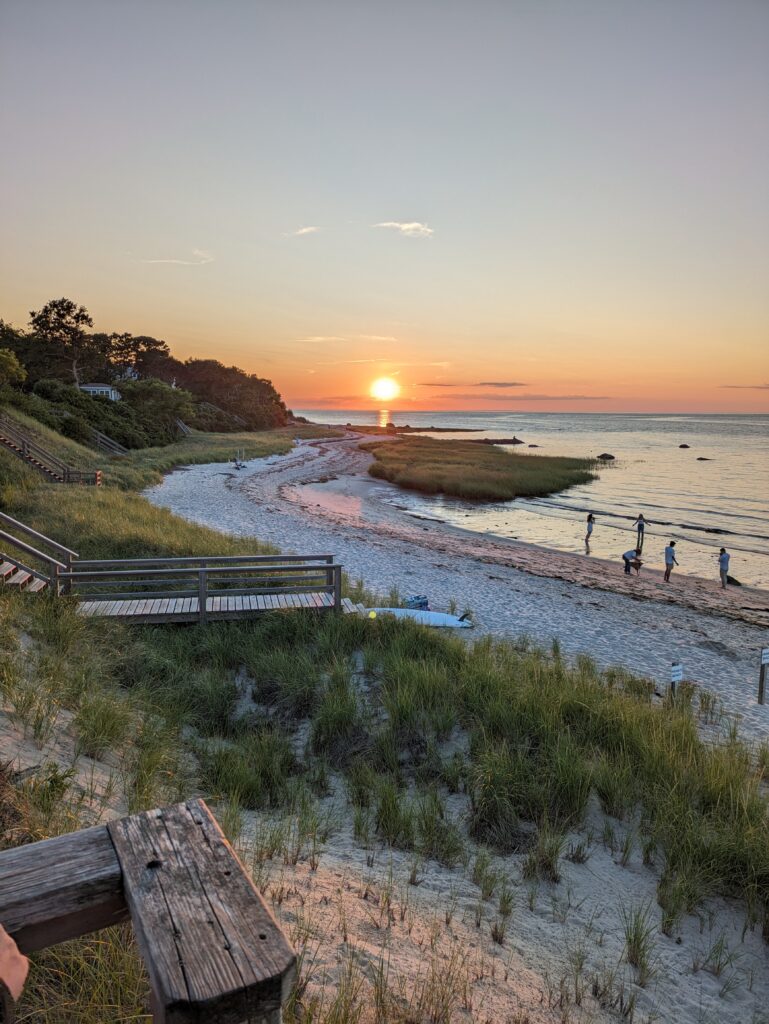 Sunset over a quiet beach with dunes and boardwalk.