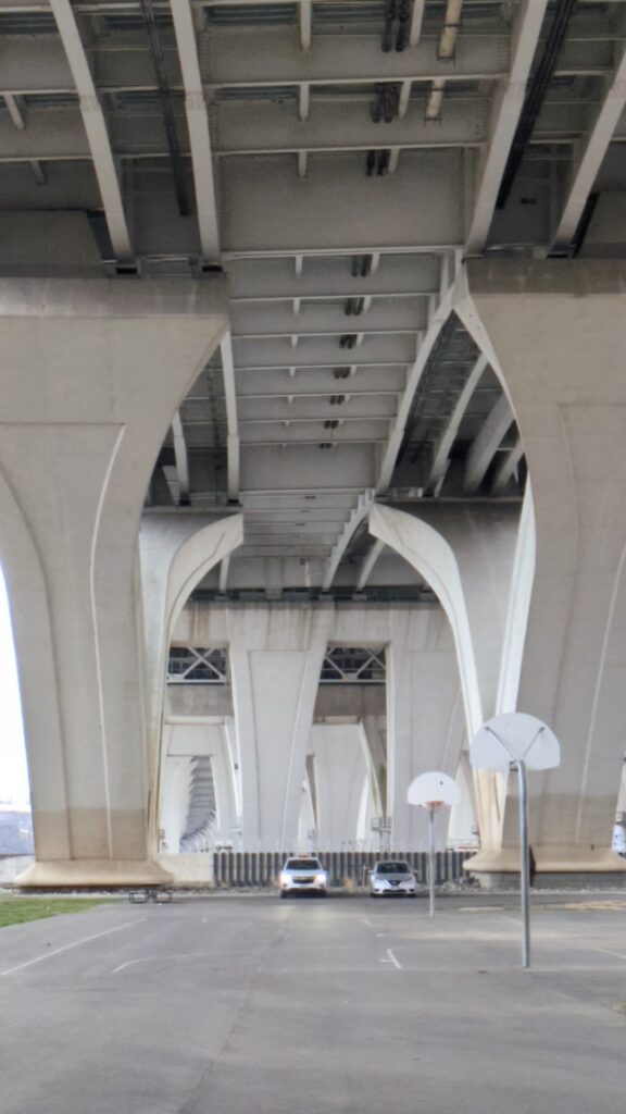 Basketball court under a massive concrete highway overpass.