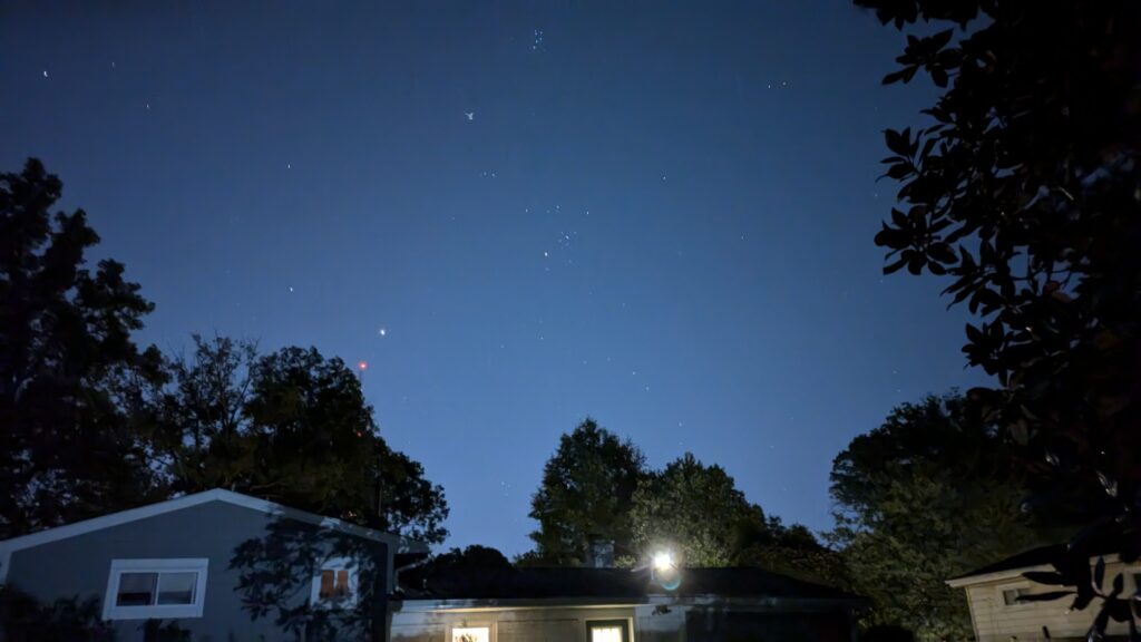 The Big Dipper visible over suburban rooftops at night.