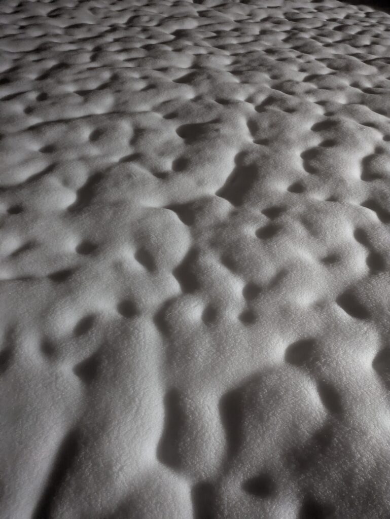 A pockmarked field of snow with deep shadows.