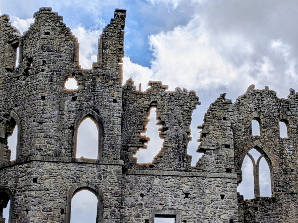 Crumbling stone castle ruins with arched windows against clouds.