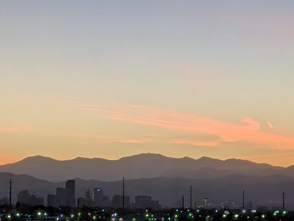 Denver skyline silhouetted against the Rocky Mountains at sunset.
